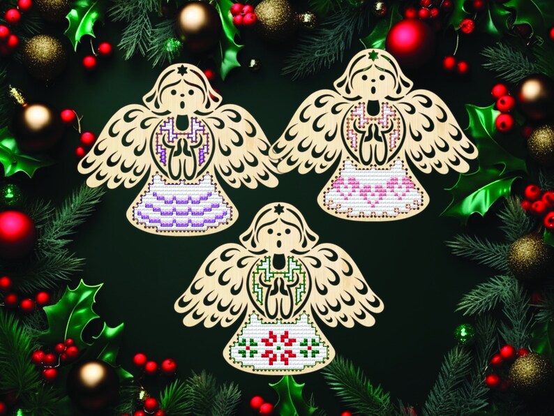 Peut inclure: Trois ornements en bois en forme d'ange avec des motifs de point de croix. Chaque ange pr&eacute;sente une palette de couleurs diff&eacute;rente : violet, rose et vert. Les anges sont entour&eacute;s de d&eacute;corations de No&euml;l, dont du houx, du pin et des boules.