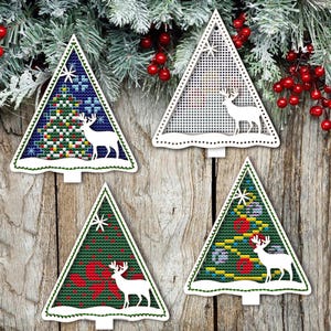 May include: Four white wooden Christmas tree ornaments with a white reindeer and a colorful Christmas tree design inside each. The ornaments are hanging on a wooden background.