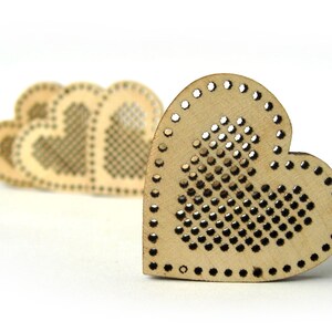 May include: A set of four unfinished wooden heart-shaped ornaments with a grid pattern for cross-stitch embroidery. The hearts are arranged in a row, with the largest heart in the foreground.