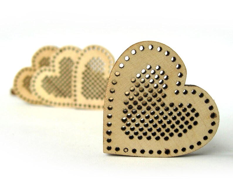 May include: A set of four unfinished wooden heart-shaped ornaments with a grid pattern for cross-stitch embroidery. The hearts are arranged in a row, with the largest heart in the foreground.