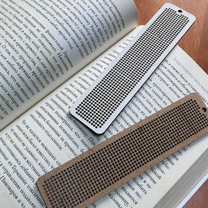 Peut inclure: Trois marque-pages en bois brun avec un motif de grille de trous. Les marque-pages sont de tailles diff&eacute;rentes et sont pos&eacute;s sur un livre ouvert.