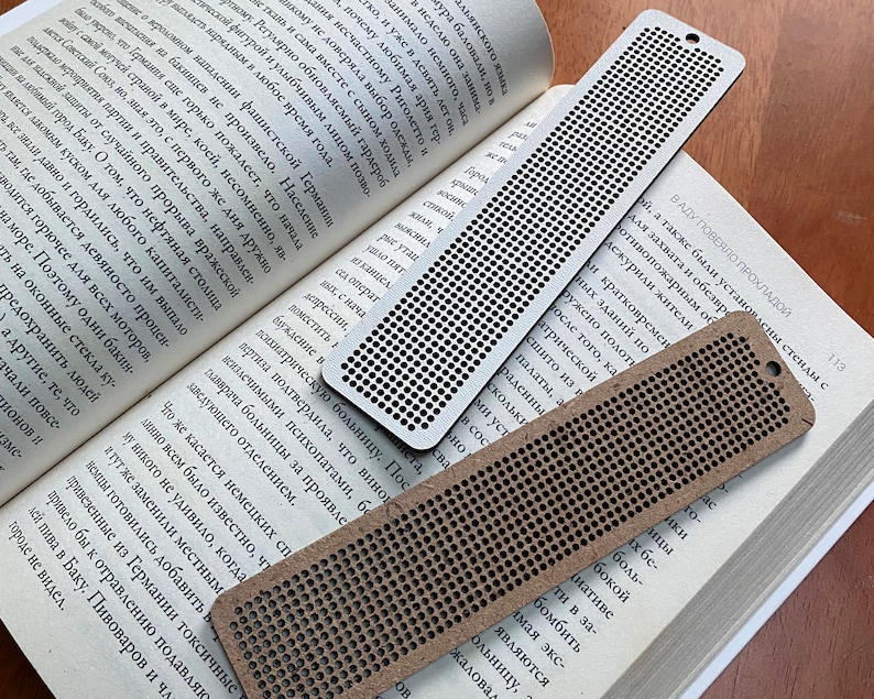 Peut inclure: Trois marque-pages en bois brun avec un motif de grille de trous. Les marque-pages sont de tailles diff&eacute;rentes et sont pos&eacute;s sur un livre ouvert.