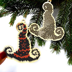 May include: Two wooden Christmas ornaments, one shaped like a witch's hat and the other like a cat. Both ornaments are decorated with black and orange cross-stitch designs.