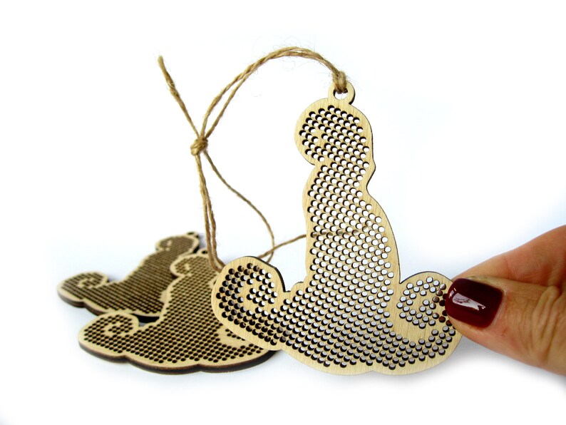 May include: Three unfinished wooden ornaments shaped like a bear, with a grid pattern for cross-stitching. The ornaments are strung together with twine.