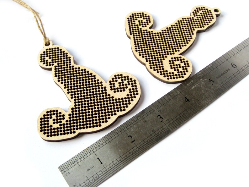 May include: Two unfinished wooden ornaments shaped like a seahorse, each with a hole for hanging. The ornaments are approximately 2 inches tall and are shown next to a ruler.