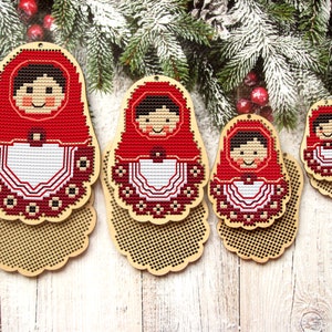 May include: Four wooden nesting dolls with red and white embroidered designs. The dolls are in various sizes and are arranged in a row on a white wooden surface.
