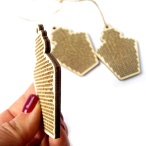 May include: Two unfinished wooden ornaments shaped like a house with a grid pattern for cross-stitching.