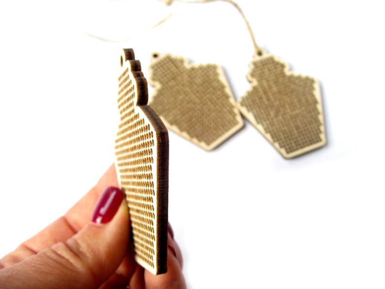 May include: Two unfinished wooden ornaments shaped like a house with a grid pattern for cross-stitching.