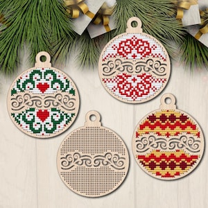 Peut inclure: Quatre formes d'ornements de Noël en bois avec un trou en haut pour accrocher. Chaque ornement a un motif brodé différent en fil rouge, vert, blanc et jaune. Les motifs comprennent des cœurs, des volutes et des motifs géométriques.