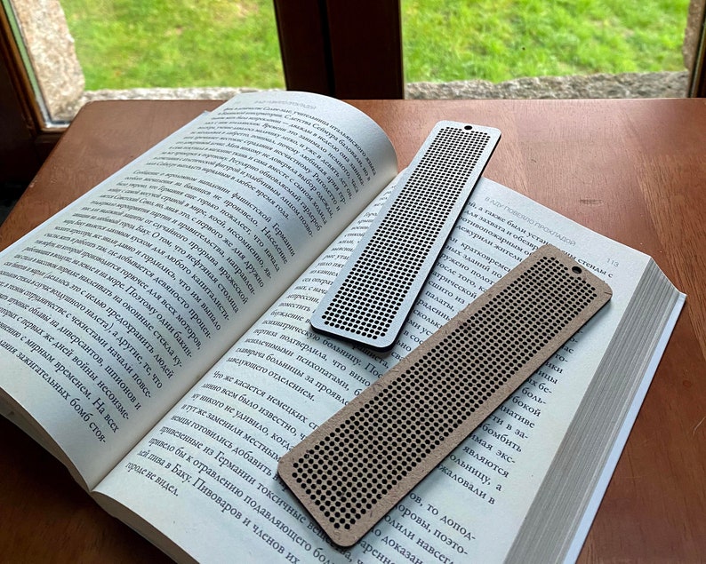 Peut inclure: Trois marque-pages en bois avec un motif en grille. Les marque-pages sont sur un livre avec du texte en russe. Les marque-pages sont de diff&eacute;rentes nuances de brun.