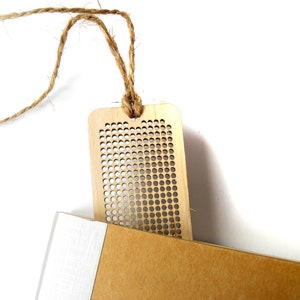 Peut inclure: Un marque-page en bois avec un motif en grille et une ficelle en ficelle brune attach&eacute;e. Le marque-page est pos&eacute; sur une surface brune.