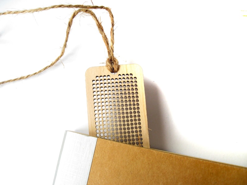 Peut inclure: Un marque-page en bois avec un motif en grille et une ficelle en ficelle brune attach&eacute;e. Le marque-page est pos&eacute; sur une surface brune.