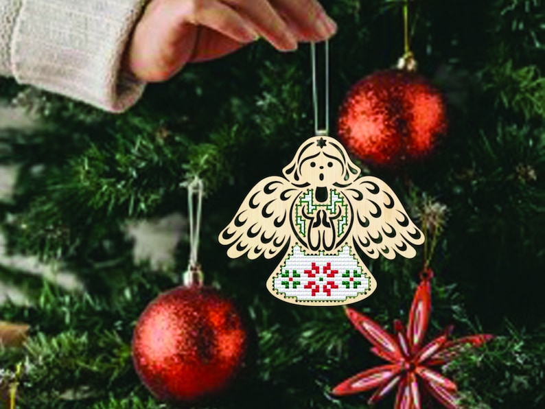 Peut inclure: Ornement de No&euml;l en forme d'ange en bois avec un design d&eacute;taill&eacute;. L'ange a des ailes d&eacute;ploy&eacute;es et une robe &agrave; motifs avec des accents rouges et verts. L'ornement est suspendu &agrave; un sapin de No&euml;l avec des boules rouges.
