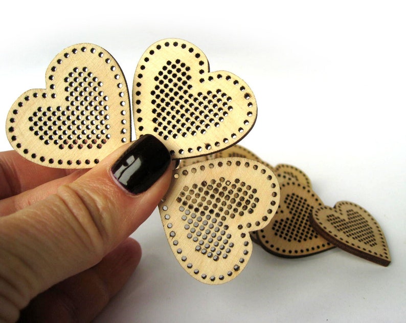 May include: A set of five unfinished wooden heart-shaped ornaments with a grid pattern for cross-stitch embroidery.
