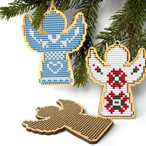 May include: Wooden angel ornaments with cross-stitch designs in blue and red, with a blank wooden angel ornament. The angels are hanging from a green pine branch, perfect for Christmas decorations.