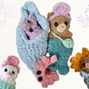 May include: A selection of handmade crochet toys, including a bunny in a blue cocoon, a bear with a mermaid tail, a white bunny, a pink bunny, and a lion. The toys are made with soft, textured yarn and have detailed facial features.