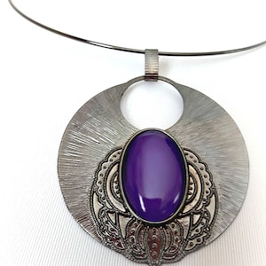 May include: A silver necklace with a large, round pendant featuring a purple gemstone set in an intricate design.