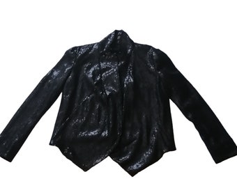 May include: A black sequined blazer with long sleeves. The jacket has a draped, open front design. The fabric has a shiny, reflective quality. The blazer is a formal garment.