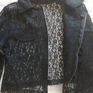 May include: Black lace jacket with a collared neckline, a front zipper, and a single pocket. The jacket's intricate floral lace pattern is visible throughout, creating a delicate and textured appearance. The jacket is a stylish outerwear option.