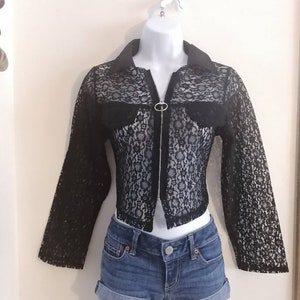 May include: A black lace jacket with a collar and long sleeves, paired with denim shorts. The jacket has a zipper closure and is displayed on a mannequin. The shorts are cuffed at the hem.