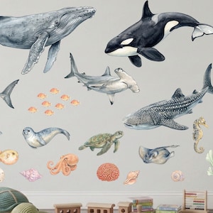 Op de afbeelding: Waterverf muurstickers met verschillende zeedieren, waaronder een walvis, orka, haaien en een zeeschildpad. Decoratieve elementen zijn koraal, schelpen en een pluche schildpad. Een houten treinset en ander speelgoed zijn ook aanwezig.