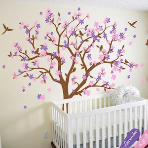 Op de afbeelding: Een bruine boom met roze en paarse bloemen en kleine vogels, een wit babybedje met een wit dekentje en drie kleurstalen met de labels "Lavendel", "Zacht roze" en "Bruin".