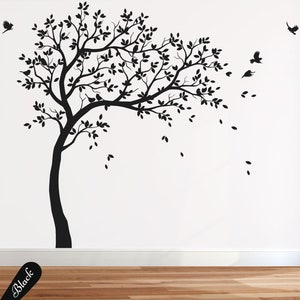 Könnte beinhalten: Schwarze Silhouette Wandaufkleber eines Baumes mit Blättern, die im Wind wehen. Der Baum befindet sich an einer weißen Wand mit einem Holzboden. Kleine Vögel fliegen um den Baum herum.