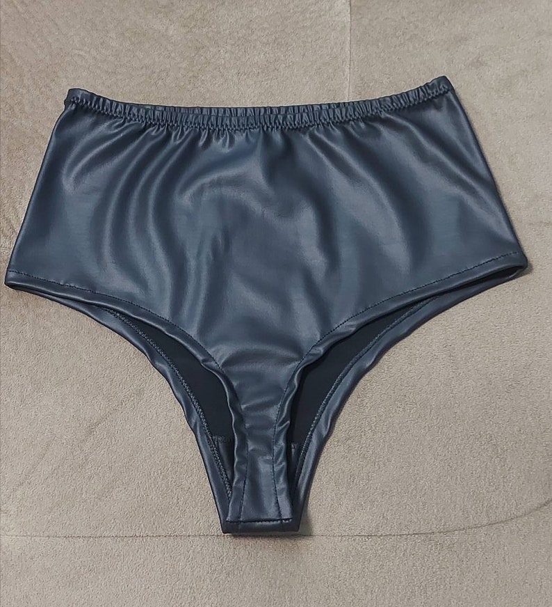 Puede incluir: Ropa interior de talle alto confeccionada en material de piel sint&eacute;tica de color gris carb&oacute;n oscuro. La prenda presenta un acabado mate y liso con una cintura el&aacute;stica fruncida y aberturas de pierna cosidas, ofreciendo una silueta estructurada.
