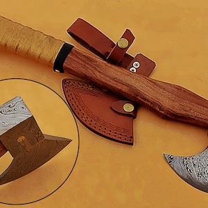 May include: A hand-forged Damascus steel axe with a wooden handle and a leather sheath. The axe has a unique pattern on the blade and a brass accent.