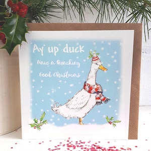 May include: A Christmas card with a cartoon duck wearing a hat and scarf, with the text "Ay up duck Have a Quacking Good Christmas" on a light blue background with snowflakes. Holly and berries are in the corners.