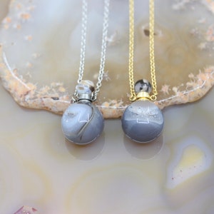 Könnte beinhalten: Zwei silberne und goldene Halsketten mit Anhängern aus Achat. Die Anhänger sind rund und haben ein graues und weißes Farbmuster.