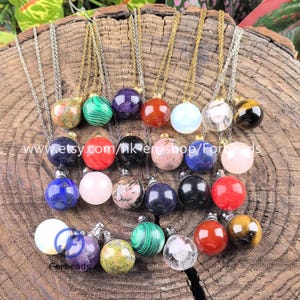 Może przedstawiać: Kolekcja wisiorków w kształcie kuli z kamieni szlachetnych na srebrnych i złotych łańcuszkach. Kule są w różnych kolorach, w tym czerwonym, zielonym, fioletowym i czarnym. Wisiorki są prezentowane na teksturowanej drewnianej powierzchni. Widoczny jest tekst "www.etsy.com/hk-en/shop/Forbeads".