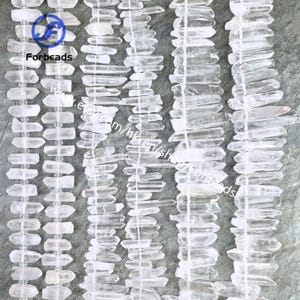 May include: Close-up of clear quartz crystal beads. The beads are of varying shapes and sizes, strung together with white thread. The image is taken from above, highlighting the texture and clarity of the crystals. The logo "Forbeads" is visible in the upper left corner.