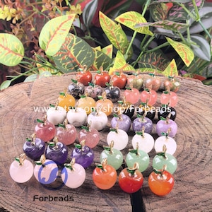 May include: A selection of gemstone apple charms in diverse colours, such as red, orange, green, purple, and white. Each apple features a gold-coloured stem and green leaf. The word "Forbeads" is at the bottom.