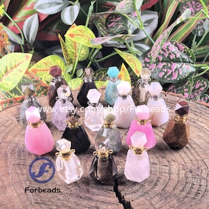 Könnte beinhalten: Eine Sammlung kleiner, dekorativer Parfümflaschen mit facettierten Edelsteinverschlüssen. Die Flaschen sind in verschiedenen Farben erhältlich, darunter Rosa, Schwarz und Klar, und sind auf einer Holzoberfläche angeordnet. Der Text "Forbeads" ist enthalten.