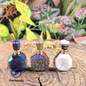 May include: Three gemstone pendant necklaces. The pendants are faceted, with a variety of colors including blue, purple, and white. Each pendant is attached to a gold-colored chain. The necklaces are displayed on a wooden surface.