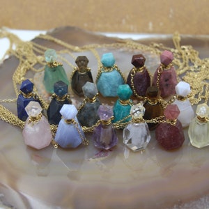 Pode incluir: Uma coleção de 18 frascos de perfume de pedras preciosas em correntes douradas. Os frascos são feitos de vários tipos de pedras preciosas, incluindo ametista, quartzo rosa e quartzo transparente. Cada frasco tem uma rolha dourada e uma corrente dourada.