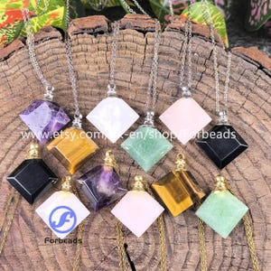 Puede incluir: Una colección de collares con colgantes de piedras preciosas en varios colores, incluyendo amatista, blanco, ojo de tigre, verde, rosa y negro. Cada colgante tiene forma de diamante y cuelga de una cadena plateada. Los collares se exhiben sobre una superficie de madera. El texto "www.etsy.com" y "Forbeads" es visible.