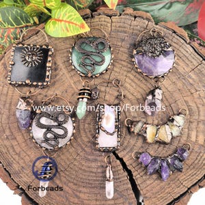 May include: A collection of assorted metal-framed gemstone pendants and connectors featuring various shapes including squares, circles, and crescents. The pieces incorporate decorative metal snakes, sun motifs, and dangling crystal points with the text www.etsy.com/shop/Forbeads.