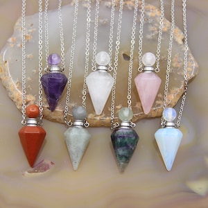 May include: Eight silver chain necklaces with crystal point pendants. Each pendant is a small bottle with a stopper. The crystals are amethyst, clear quartz, rose quartz, red jasper, labradorite, green fluorite, and opal.
