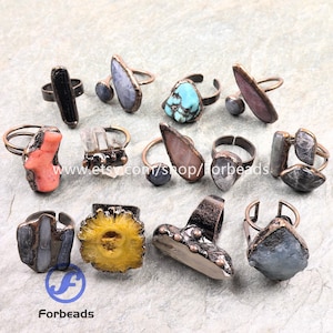 May include: A selection of handcrafted rings with diverse gemstones, such as turquoise, quartz, and coral. The rings have copper-toned metal settings and unique stone shapes. The image includes the text "Forbeads" and a website address.