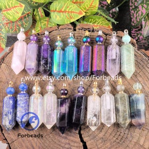 Puede incluir: Una colección de botellas de aceites esenciales de piedras preciosas en varios colores, incluyendo rosa, morado, azul y tonos iridiscentes. Cada botella tiene una tapa de metal y un fondo puntiagudo. Las botellas están sobre una superficie de madera.