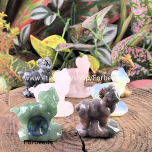Könnte beinhalten: Eine Sammlung von Widder-Figuren aus Edelsteinen in verschiedenen Farben, darunter Grün, Rosa, Grau und Braun. Die Figuren werden auf einer Holzoberfläche mit Blättern im Hintergrund präsentiert. Der Etsy-Shop-Name "Forbeads" ist sichtbar.