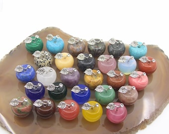 May include: A collection of 24 small, polished gemstone apples with silver leaf stems. The apples are arranged on a brown agate slice and feature a variety of colors and patterns.