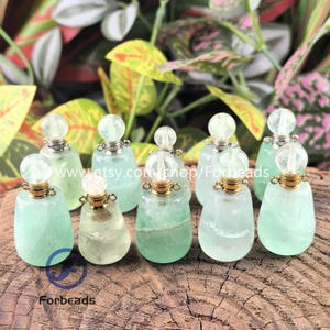 May include: A collection of small, light green gemstone bottles with clear stoppers and gold-colored accents. The bottles are displayed on a wooden surface, with foliage in the background. The text "www.etsy.com/shop/Forbeads" is visible.