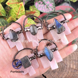 May include: A selection of gemstone pendants with rose quartz and labradorite stones. Each pendant has a unique shape and colour, with a wire loop for hanging. The Etsy shop name "Forbeads" is visible.