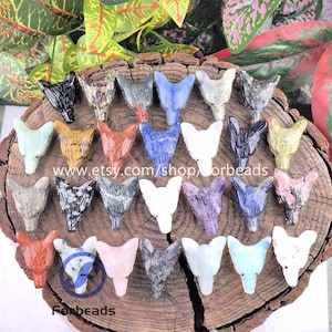 May include: A selection of carved stone fox head pendants in diverse colours, such as black, white, blue, and orange. The pendants are arranged on a wooden surface. The Etsy shop URL is visible in the image.