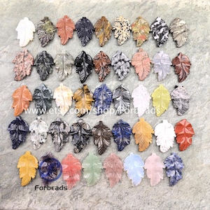 Può includere: Una collezione di ciondoli a forma di foglia in pietra scolpita in vari colori e motivi. Le foglie sono finemente dettagliate, con una varietà di colori tra cui bianco, nero, marrone e blu. Il nome del negozio Etsy "Forbeads" è visibile.
