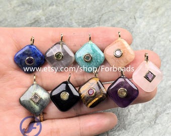 May include: A collection of gemstone pendants in various colors, including blue, gray, and pink, each with a gold-colored bail. The pendants are square-shaped with a smaller, circular stone in the center. The Etsy shop name "Forbeads" is visible.