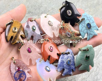 May include: A collection of gemstone pendants in the shape of a hand, each with a gold-colored bail and a small, central stone. The pendants are various colors, including tiger's eye, black, pink, and blue. The Etsy shop name "Forbeads" is visible.
